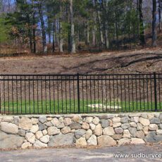 Aluminum Wrought Iron Fence by Sudbury Cedar Fence sits near a stone wall in Sudbury, MA