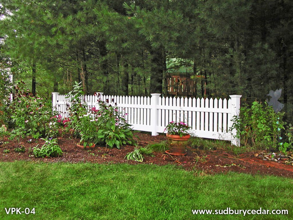 Decorative white vinyl picket fence installed alongside landscaped garden bed and residential walkway in Massachusetts.