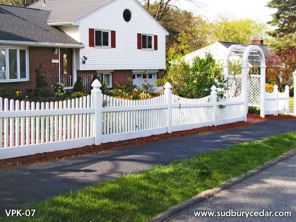 Decorative white vinyl arbor with curved vinyl picket fencing installed in landscaped Massachusetts residential yard.