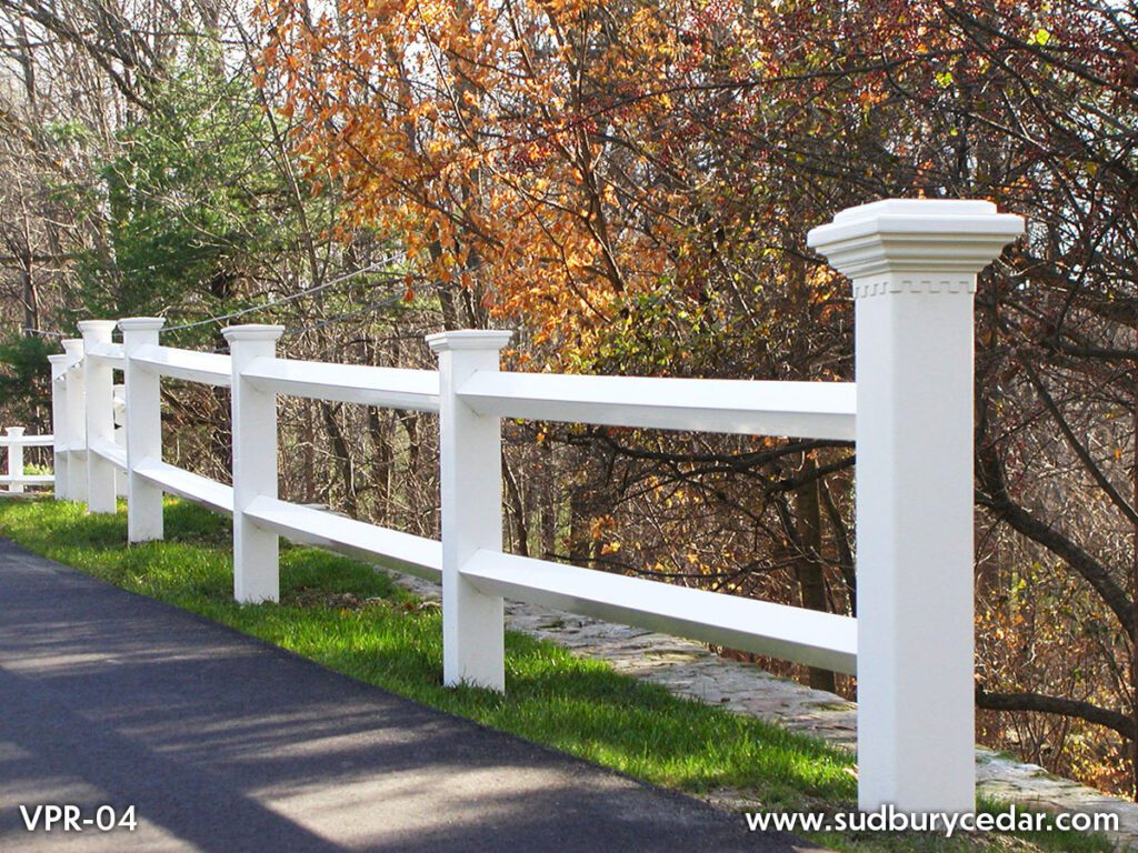 White vinyl post and rail fence installed along landscaped residential property boundary in Massachusetts.