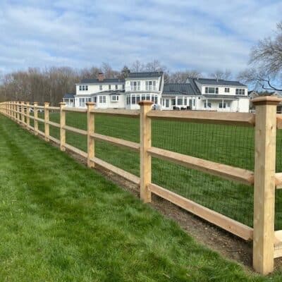 Northern white cedar post and rail fence with wire mesh enclosure on large residential lawn in Harvard Massachusetts