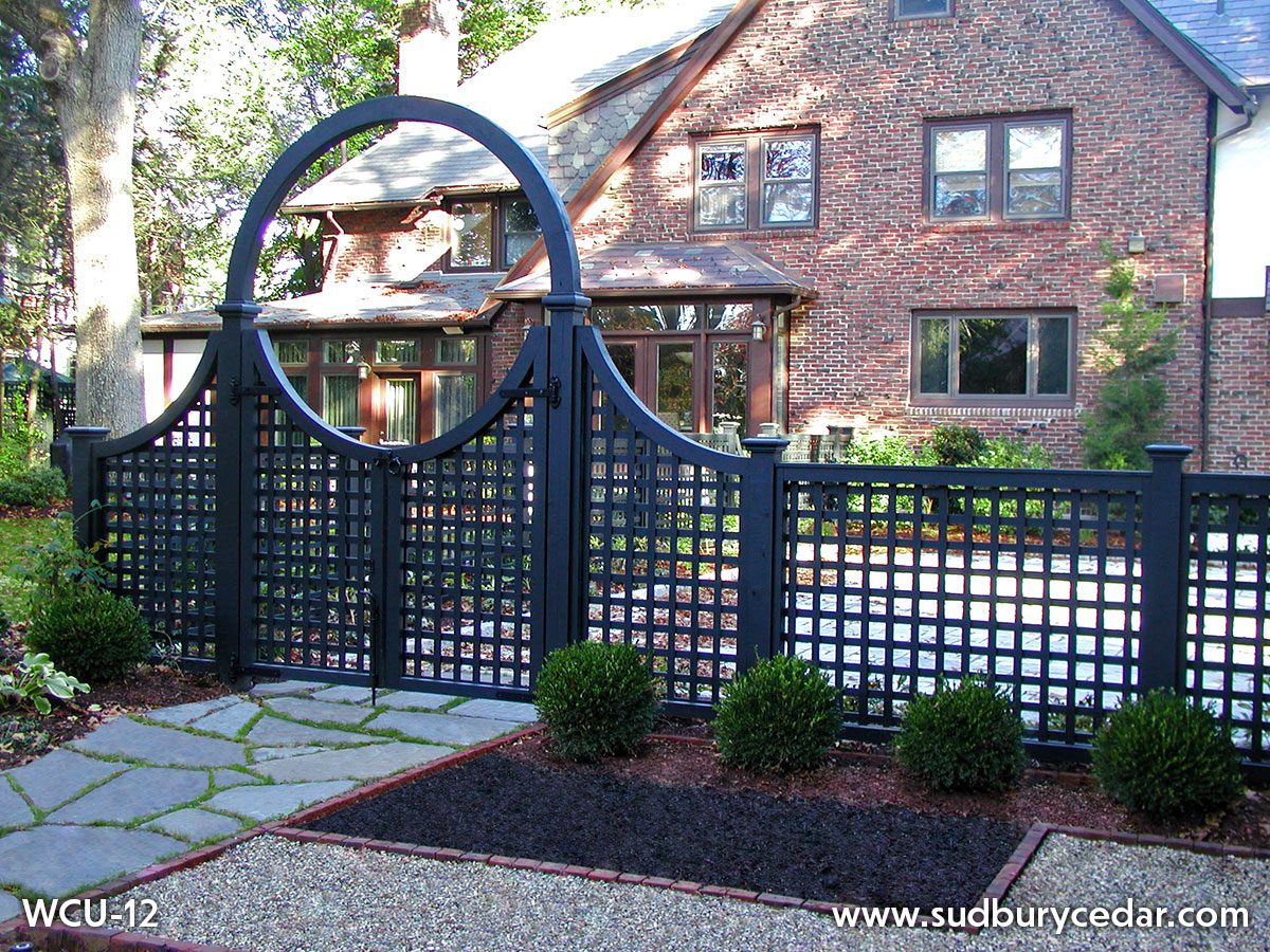 Black lattice fence with an arched gate in front of a brick home, showcasing an elegant fence design that complements the home’s architecture MetroWest Massachusetts