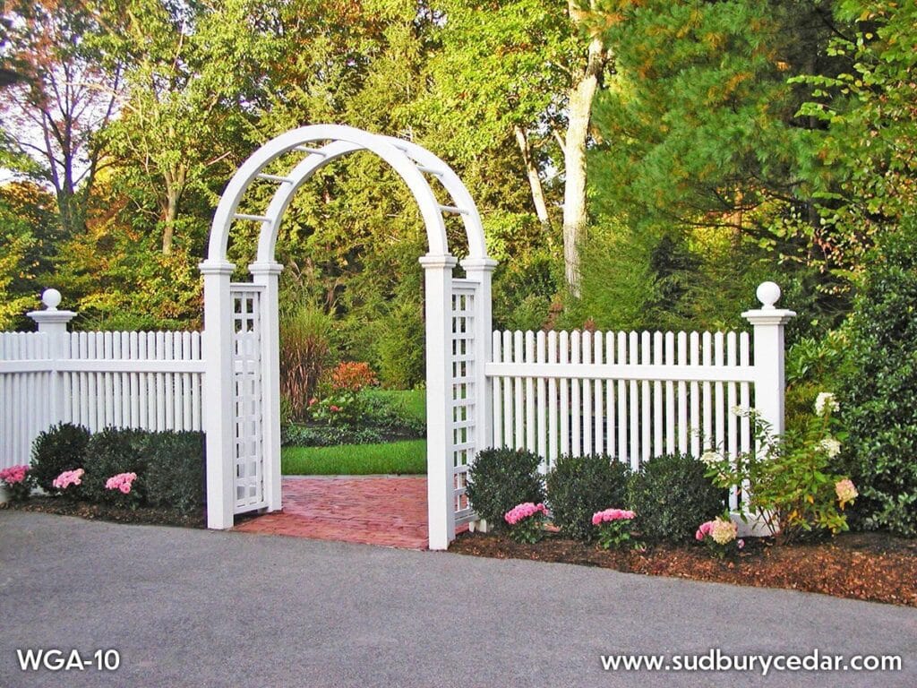 Decorative white picket fence with arbor gate and lattice panels in landscaped yard in MetroWest MA