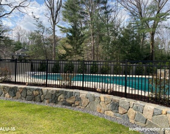 Black aluminum pool fence surrounding an in-ground swimming pool with decorative ornamental pickets and open backyard visibility.