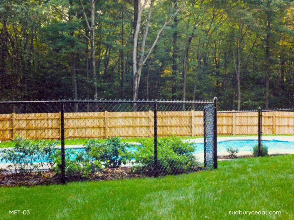 Black vinyl-coated chain link fence enclosing a backyard pool area with landscaped lawn in Massachusetts
