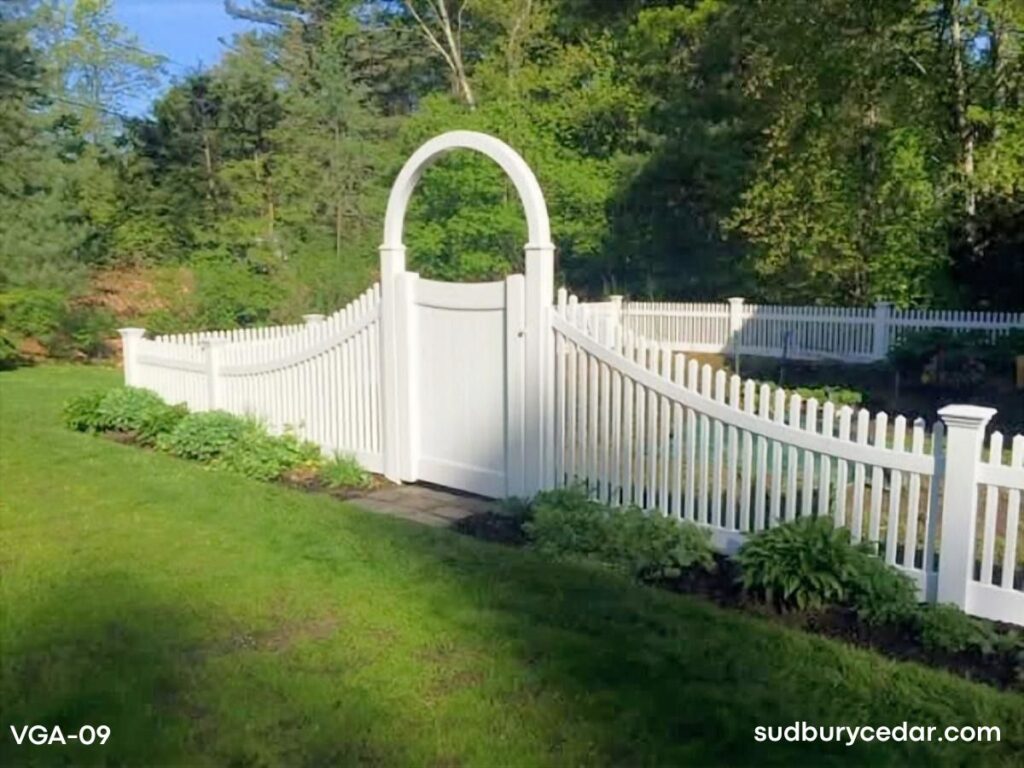 Curved white vinyl picket fence with decorative arbor gate installed in landscaped backyard in Massachusetts.