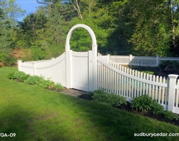 Curved white vinyl picket fence with decorative arbor gate installed in landscaped backyard in Massachusetts.