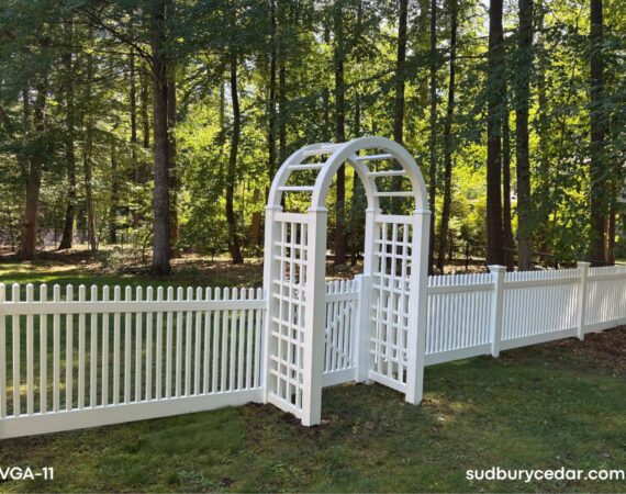 White vinyl arbor gate with lattice side panels and matching vinyl picket fencing installed in wooded Stow, Massachusetts backyard.