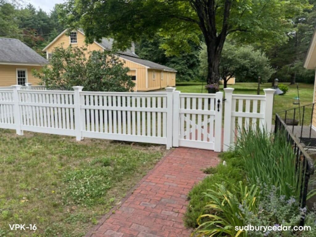 White vinyl picket fence installed along residential walkway with landscaped front yard and garden entrance in Sudbury, Massachusetts.