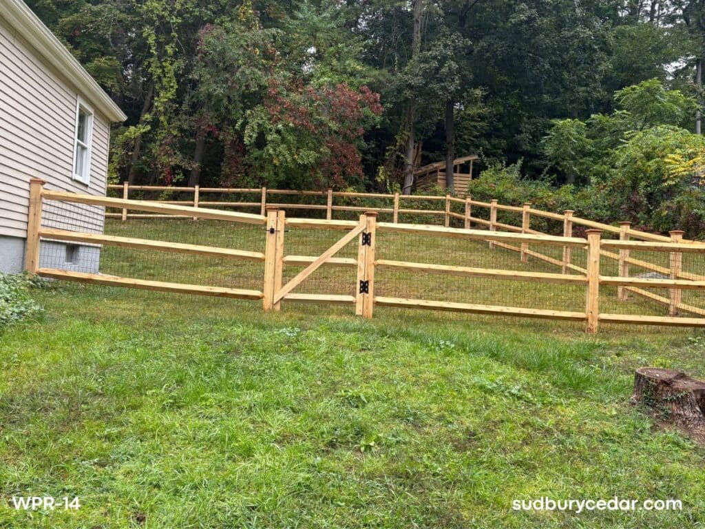 cedar post and rail fence with wire mesh and gate installed on sloped backyard in sudbury ma