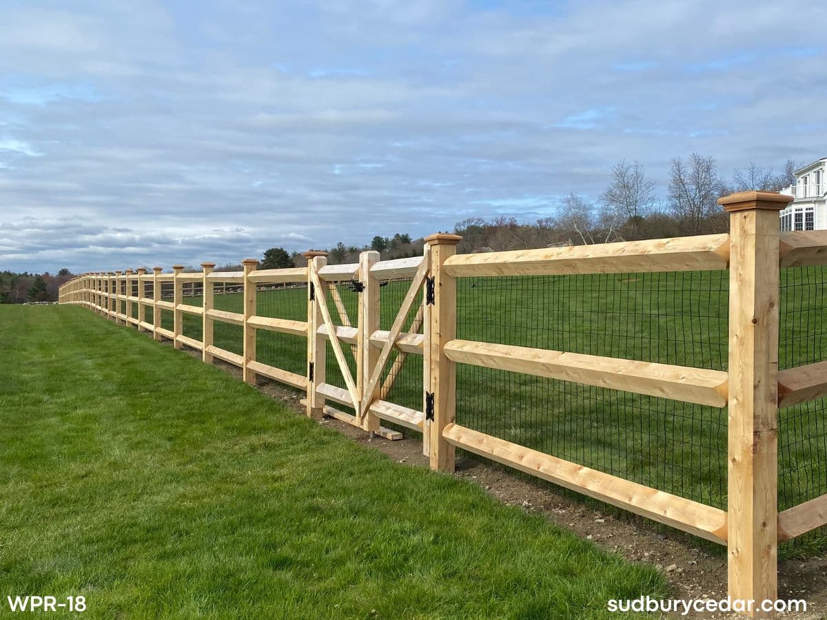 Custom cedar post and rail fence with wire mesh and gate installed for a large residential property in Harvard, Massachusetts.
