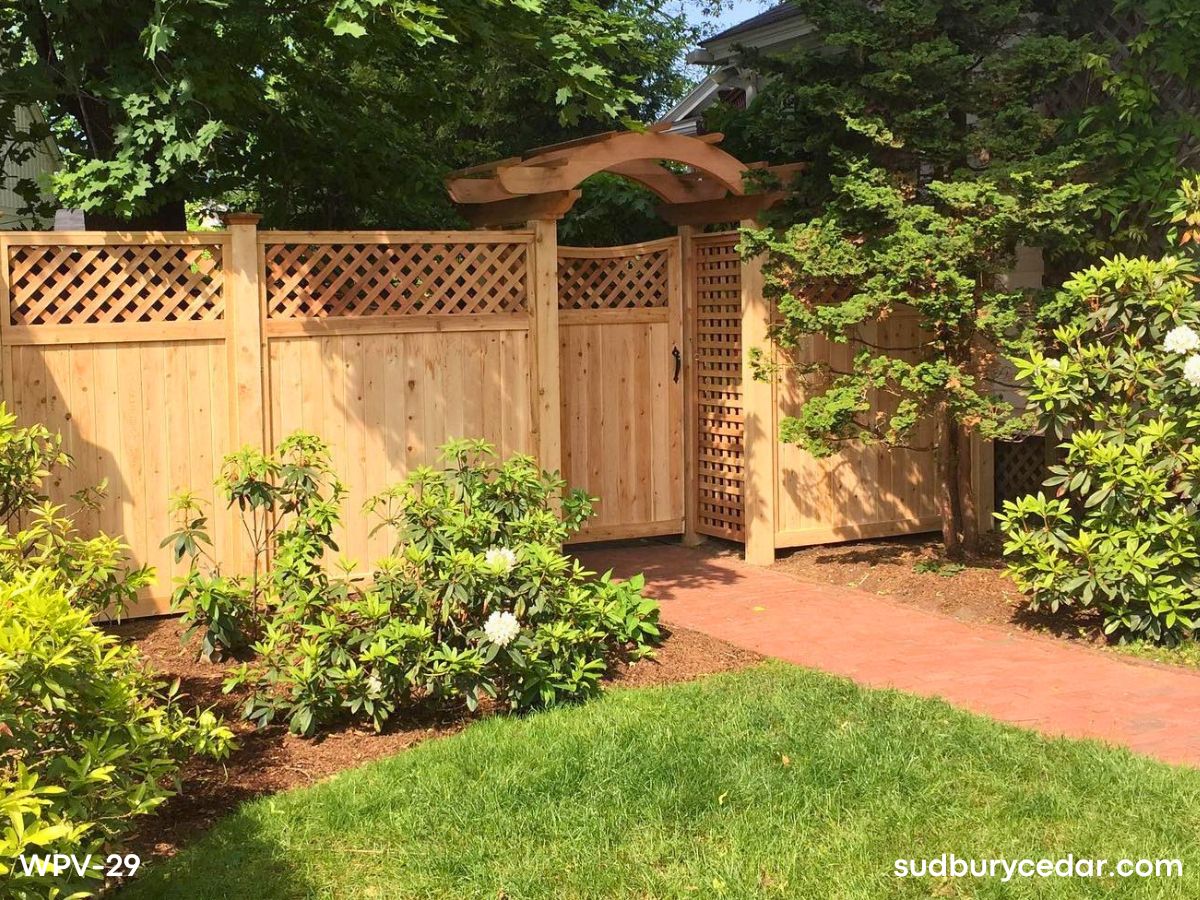Custom decorative cedar privacy fence with pergola-style arbor creating an elegant backyard entry and outdoor living space in MetroWest Massachusetts.