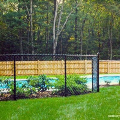 Black vinyl-coated chain link fence enclosing a backyard pool area with landscaped lawn in Hudson, Massachusetts
